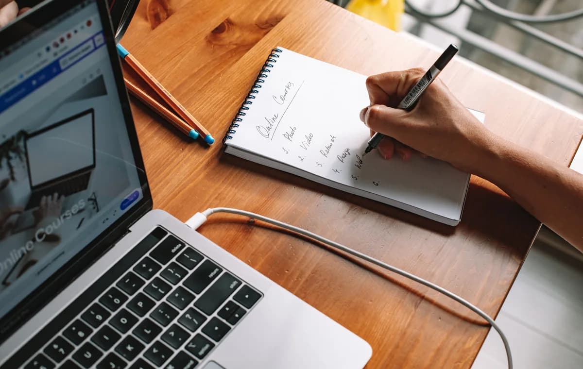 Persoon die naast een laptop een online cursus uitwerkt in een notitieboek